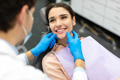 男牙医正在给一位美女检查牙齿，检查时，戴着橡胶手套的医生抚摸着病人的牙齿