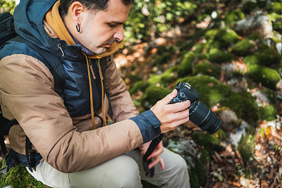一位年轻美丽的摄影师在森林里的一块石头上散步，拍摄了环境的奇观，同时看着相机里的照片