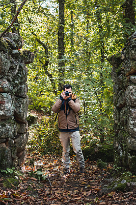 年轻美丽的摄影师从森林里的老石门拍了一张照片，看着相机，垂直照片