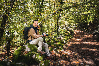 年轻而美丽的摄影师在散步和拍摄环境奇观后，在森林的一块石头上休息的侧面肖像