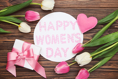 花的郁金香，心，礼盒和圆形卡片与文字妇女节快乐在棕色木制背景