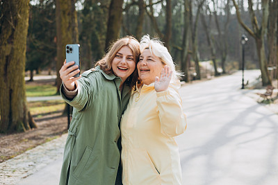 快乐的老母亲和成年女儿在城市街道上自拍。穿着得体的女性朋友户外照。两个女人在一起用手机自拍。家庭日概念。