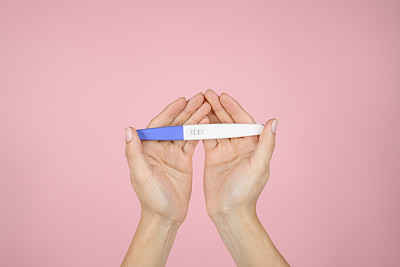一名妇女的手在一个孤立的粉红色背景上拿着一个阳性的怀孕测试。母亲的概念