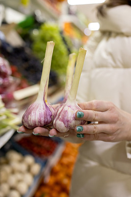 在农贸市场，一位妇女的手拿着新鲜的大蒜。正确选择食材。