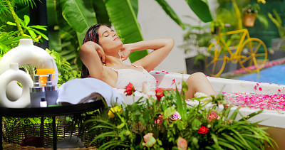 印度微笑健康的年轻成年妇女放松地坐在浴缸里，在豪华的户外度过时光。美丽的z世代可爱的女孩早上沐浴玫瑰花瓣水享受暑假度假酒店度假之旅