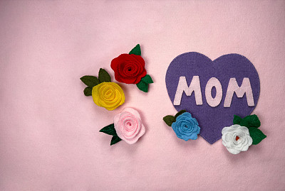 粉红色的毛毡板上写着母亲节快乐的话。母亲节作文，粉红色毛毡表面上有玫瑰和一颗紫色的心