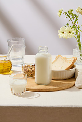 一瓶没有标签的牛奶，一杯黄豆和一碗放在砧板上的三明治。一个装满蜂蜜的罐子和一个装饰好的花盆。品牌模型