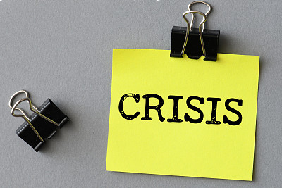 “危机”这个词写在一张黄色的小纸片上，背景是灰色的。