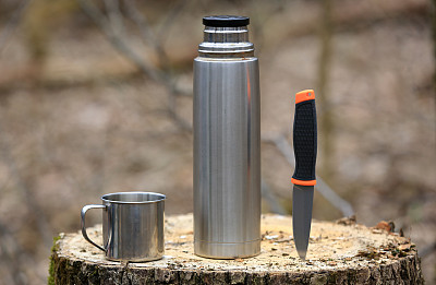 保温瓶，马克杯和小刀放在森林里的一个木桩上