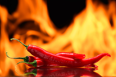 红辣椒，在燃烧的火的背景，火焰在黑色的背景，辛辣的香料