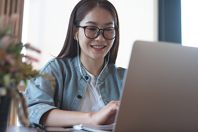 快乐的亚洲休闲商务女性在笔记本电脑上工作，通过在线会议应用程序在咖啡店进行视频会议。学生学习在线课程，电子学习，远程工作，自由职业者的生活方式