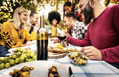 快乐的朋友在花园餐厅举行烧烤晚宴-快乐的家人坐在餐桌旁一起喝红酒-食物和饮料概念与男孩和女孩一起吃新鲜的食物