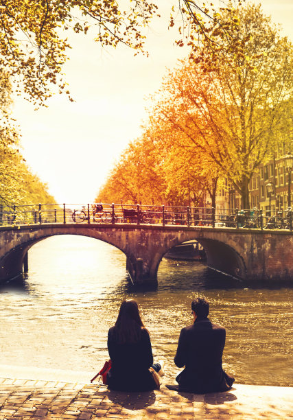 一对对朋友或恋人在运河的堤岸上放松，看着阿姆斯特丹的河流和桥梁。