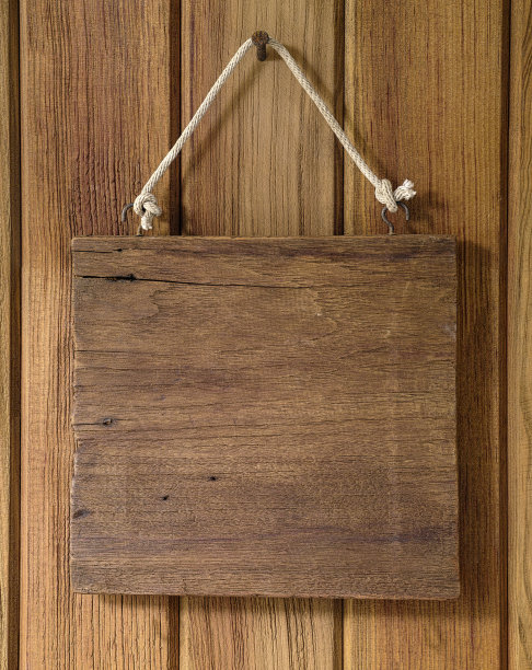 一块旧木板挂在生锈的钉子上，挂在旧的风化的木板墙的背景上。