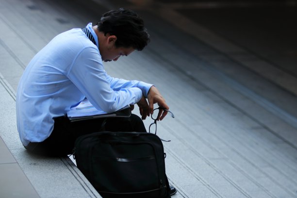 侧面的压力沮丧的年轻亚洲男子坐在楼梯上。他对某事感到失望或疲倦。