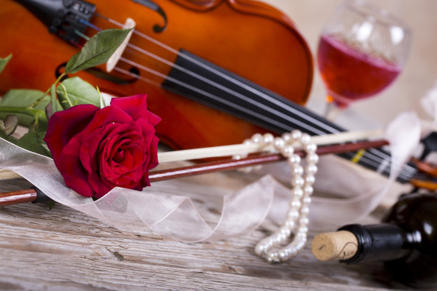 小提琴，红玫瑰，珍珠项链和酒在木桌上