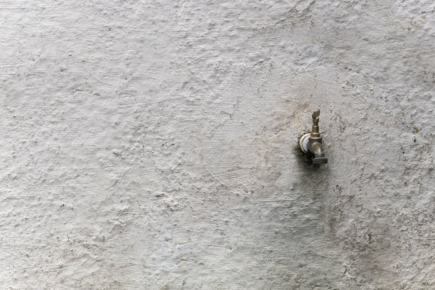 旧的和开裂的墙壁水龙头在白色油漆的水泥墙。枯燥乏味的粗糙的纹理。