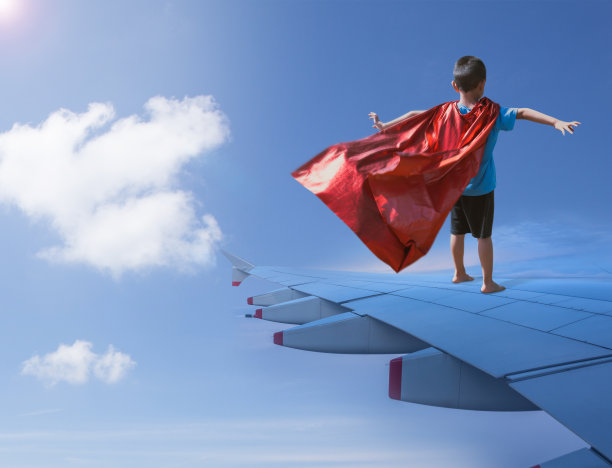 男孩打扮成超级英雄站在飞机机翼上