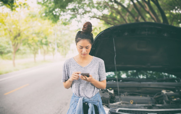 亚洲女人一边看一边用手机，压力山大的男人坐在车抛锚后的街道上