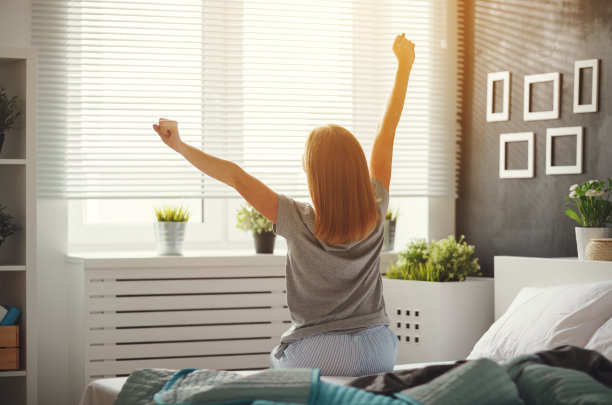 一个年轻的女人早上醒来,背对着窗边的卧室