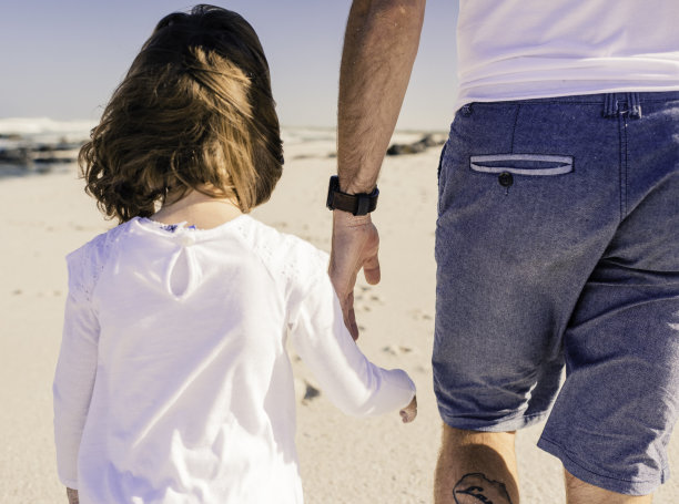 背影小女孩拉着父亲的手，他们走下海滩