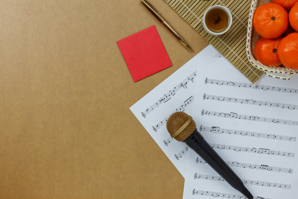表顶视图的音乐表注和附件中国新年和农历节日的概念。在现代乡村棕色木制的家庭办公办公桌上的必需品。橙色的篮子和茶和红色的口袋。