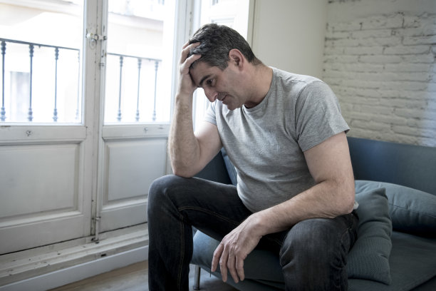 40岁或50岁悲伤和担心的人与灰色头发坐在家里的沙发上，看起来沮丧和浪费在悲伤的面部表情沮丧和生活问题的概念