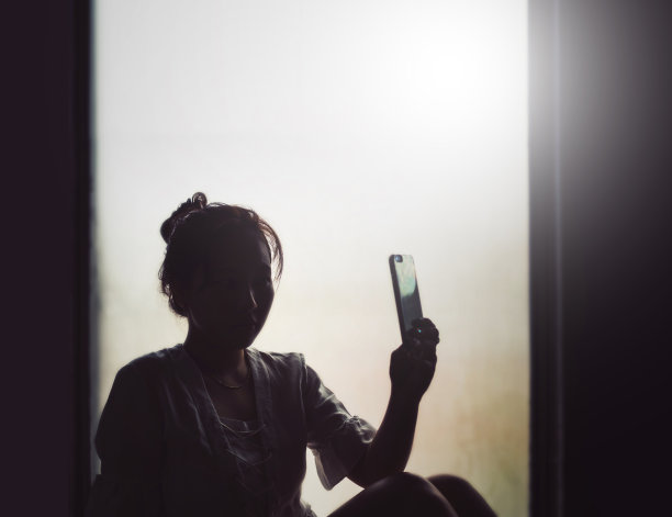 窗户上的女孩用手机自拍的剪影