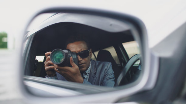 狗仔队队员坐在车里用单反相机拍照时，侧面镜中的影像