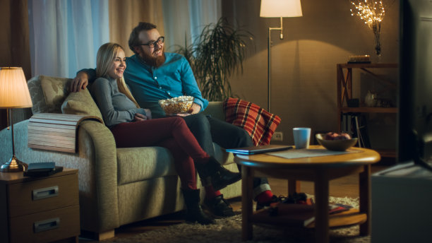 晚上，男人和女人坐在沙发上看电视和吃爆米花。客厅是舒适的。