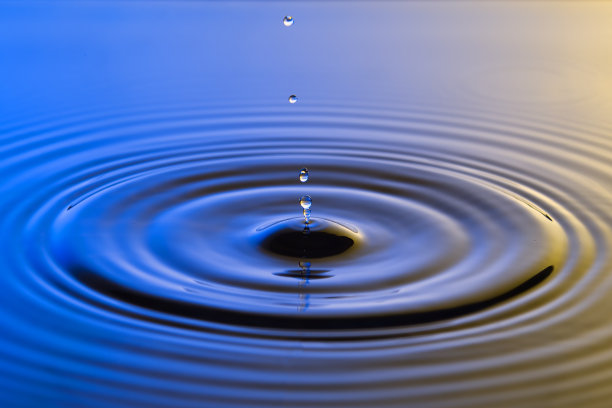 水滴近距离与同心涟漪在五颜六色的蓝色和黄色表面