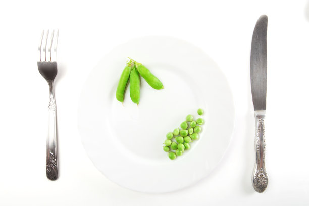 盘子里的豌豆和豆荚，刀叉分开放在白色背景上