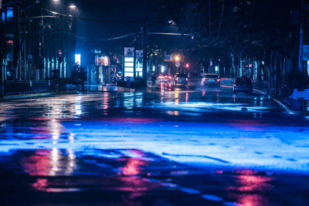 汽车在雨中行驶在潮湿的路面上，彩色的灯光反射在潮湿的柏油路上
