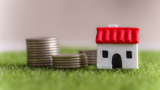 房屋和贷款概念。红色屋顶的小房子和草坪上成堆的硬币。