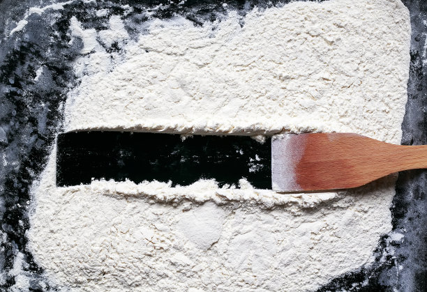 厨房的木抹刀在白色易碎的面粉背景上画了一个在黑色桌子上写字的框架