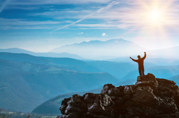一个人的剪影站在悬崖峭壁上,成功和胜利就在群山之间