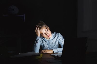 一个疲惫的女人在黑暗的办公室复印室拿着笔记本电脑