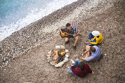朋友们在沙滩上弹吉他，围着篝火唱歌