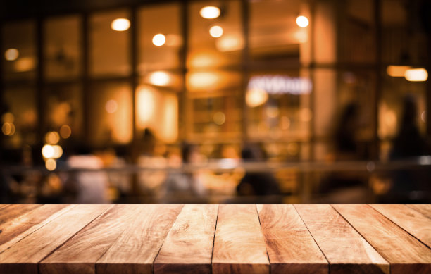木质桌面上模糊的咖啡馆(餐厅)与浅金色在黑暗的背景。用于蒙太奇产品展示或关键视觉布局。