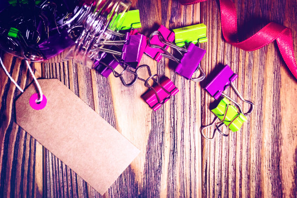 彩色回形针从罐子溢出在木制背景上.绿色,莱拉曲别针和红色蝴蝶结.