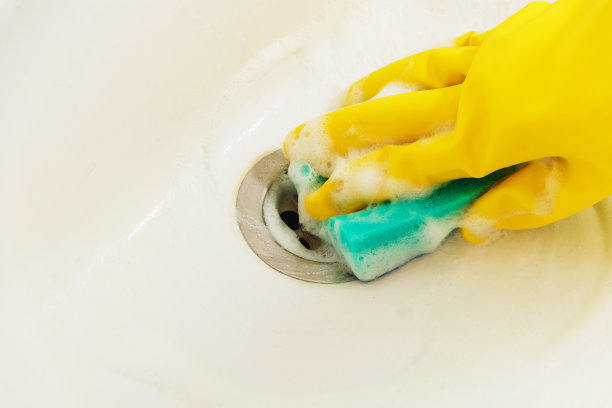 用黄色橡胶手套和蓝色海绵清洗浴室水槽-家务，春季清洁概念。
