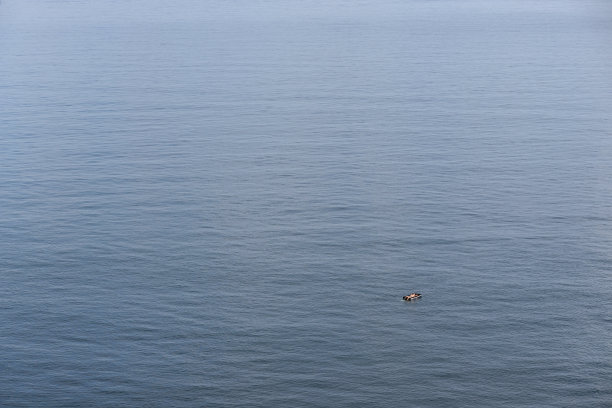广阔的海域和一个漂浮在充气床垫上的人在远处