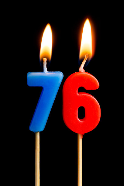 燃烧蜡烛的形式76 76(数字,日期)为蛋糕孤立在黑色的背景.