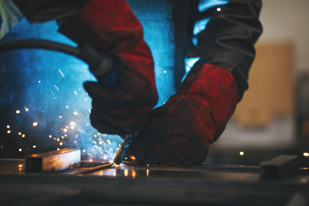 年轻的专业焊工,打磨焊接金属棒材 年轻的专业焊工,打磨焊接金属棒材