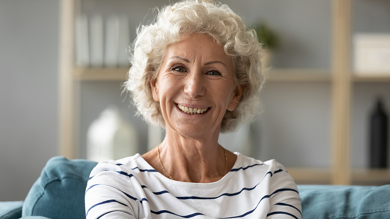 Head,shot,portrait,grey-haired,positive,elderly,woman,65,–,70,years,resting,on,couch,smiling,looking,at,camera,feels,happy,enjoy,retired,life,,having,wide,toothy,smile,dentures,dental,services,concept