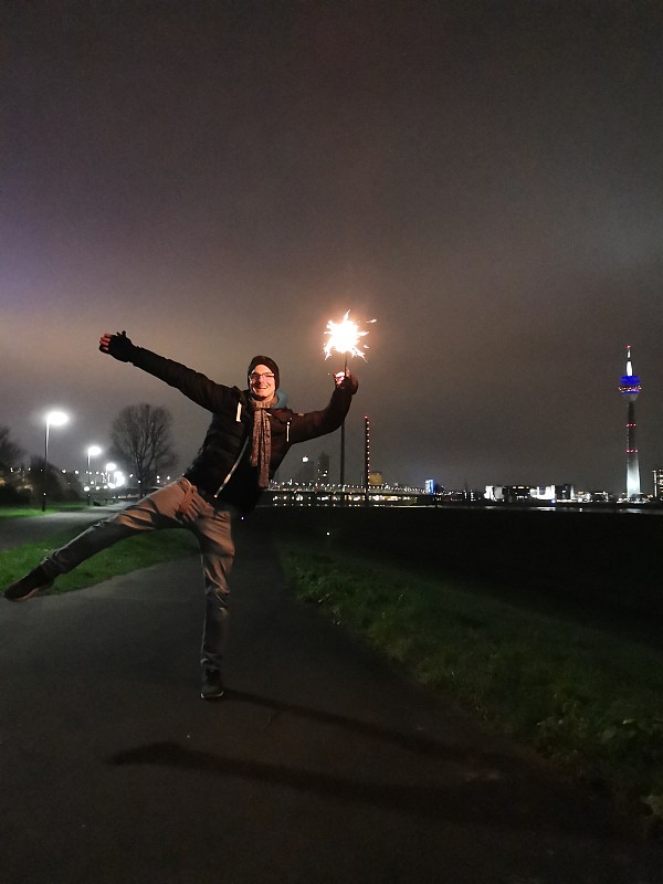 Young,man,posing,with,bright,sparkler,in,front,of,Düsseldorf',skyline,at,night