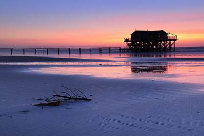 宁静的海岸日落，码头和沙滩上的棚屋