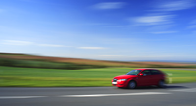红色汽车超速行驶，乡村道路穿过夏天的风景，故意模糊