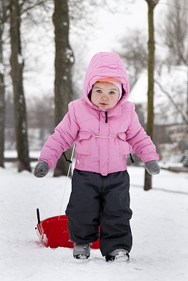 年轻的女孩穿着粉红色的衣服，在冬天拉着雪橇