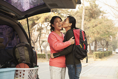 母亲和女儿在大学校园的车后拥抱